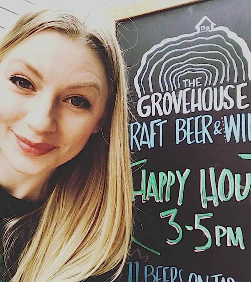 Smiling woman with the Grove House sign showcasing happy hour times